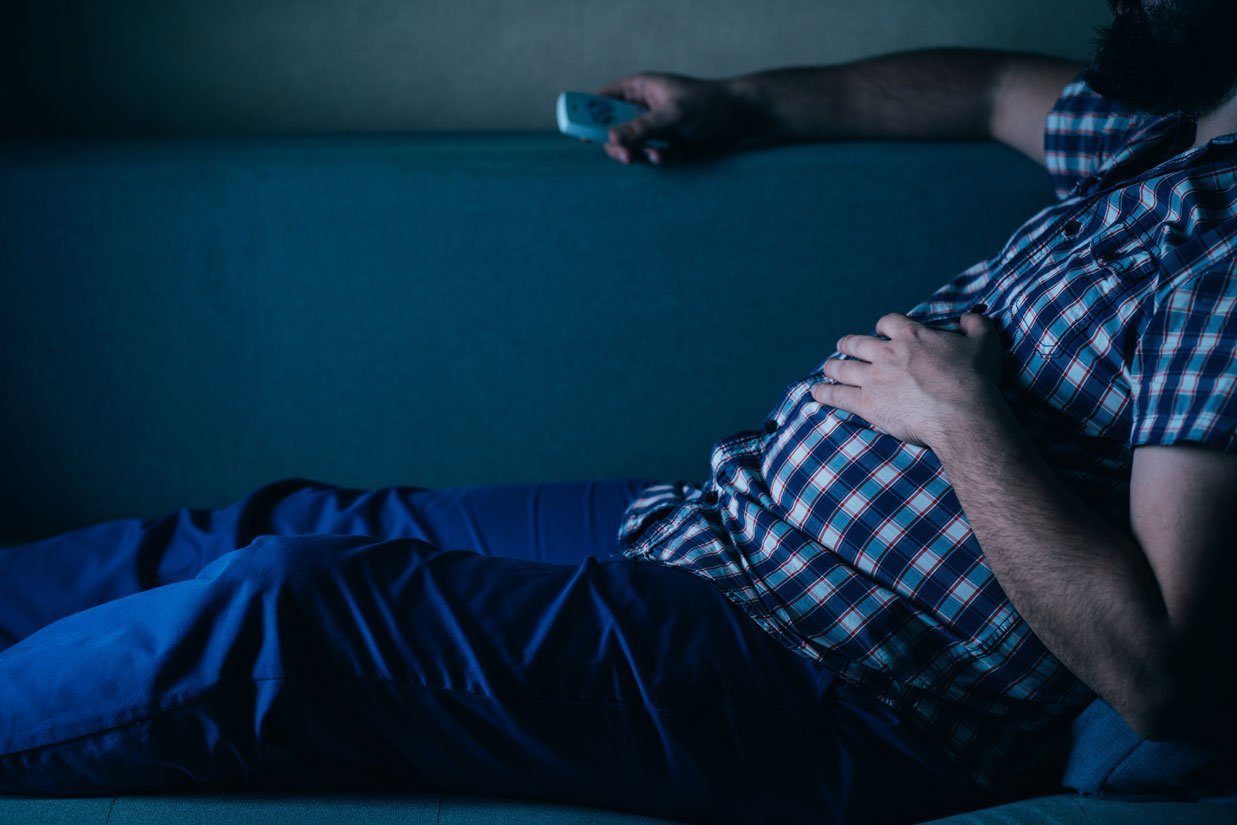 Persona en el sofá en un ambiente con poca luz; ilustra el sedentarismo y los hábitos de vida.